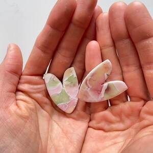 May include: Two heart-shaped pieces of pink and green marbled clay. The clay has a swirled pattern and is a light pink and green color.