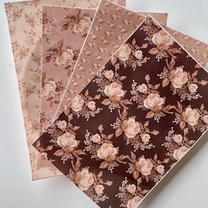 Può includere: Quattro fogli di carta con motivi floreali di rose nei toni del marrone, rosa e beige. I fogli sono disposti a ventaglio, mostrando i diversi disegni. La carta ha un'estetica vintage e romantica.