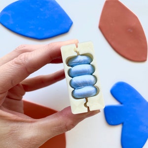 May include: A white silicone mold with four round cavities filled with light blue resin. The mold is being held in a hand.