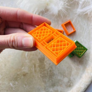 May include: Orange plastic cookie cutters shaped like windows with a diamond pattern. The cutters are on a white surface.