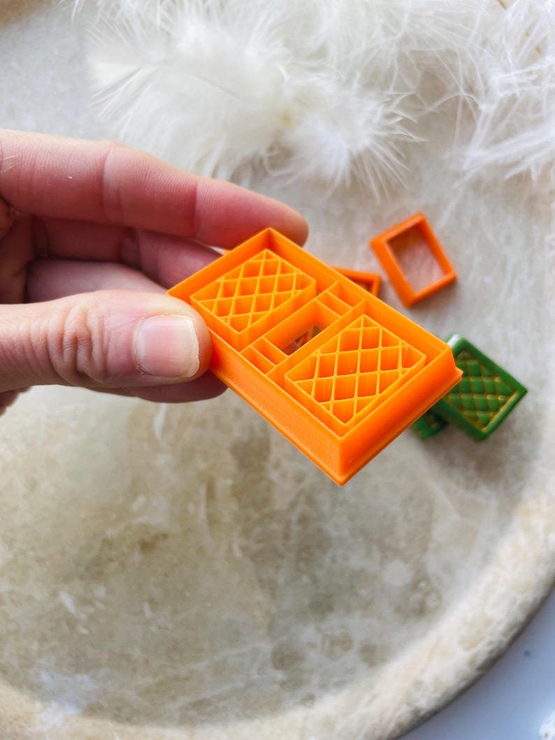 May include: Orange plastic cookie cutters shaped like windows with a diamond pattern. The cutters are on a white surface.