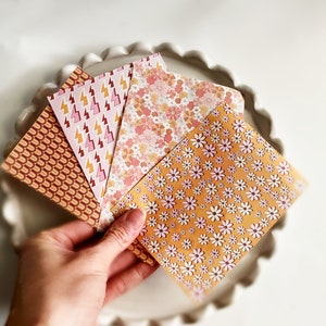 May include: Four patterned paper sheets in a variety of colors and designs. The designs include a geometric pattern, a floral pattern, a lightning bolt pattern, and a daisy pattern.