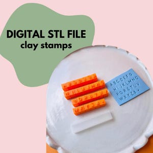 May include: Orange clay stamps with individual letter blocks, a blue square with stamped alphabet letters, and the text "DIGITAL STL FILE clay stamps" on a white plate. A clear plastic holder is also present.