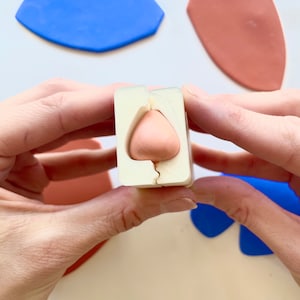 Puede incluir: Un molde de silicona blanco con una forma de corazón de arcilla rosa en su interior. El molde está abierto y el corazón de arcilla es visible.