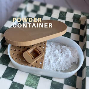 May include: A tan powder container with a lid and a perforated insert, partially filled with white powder. The container has the words "POWDER CONTAINER" in white text. The container sits on a checkered surface.