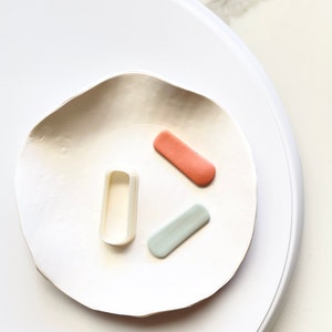 May include: Three small rectangular shapes on a white ceramic plate. The shapes are made of polymer clay and are in the colors light blue, peach, and white.
