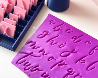 May include: A purple silicone sheet with the alphabet in cursive letters embossed into the surface. The letters are a b c d e f g h i j k l m n o p q r s t u v w x y z.