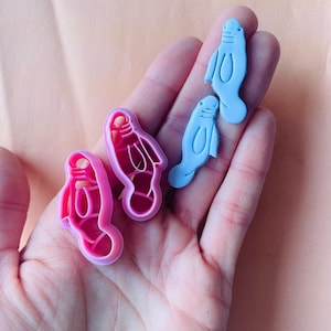 Peut inclure: Un ensemble de trois emportes-pièces, deux roses et un bleu. Les emportes-pièces roses sont en forme de paire de chaussons de ballet, et l'emporte-pièce bleu est en forme de lamantin.