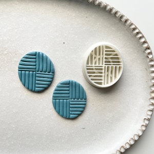 Op de afbeelding: Twee ronde oorbellen van tealblauwe polymer klei met een geometrisch patroon. De oorbellen liggen op een wit keramiek bord met een witte plastic mal.