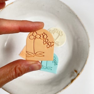 Photo of a polymer clay earring featuring an embossed orchid. At the back is the clay stamp used to emboss the flower.