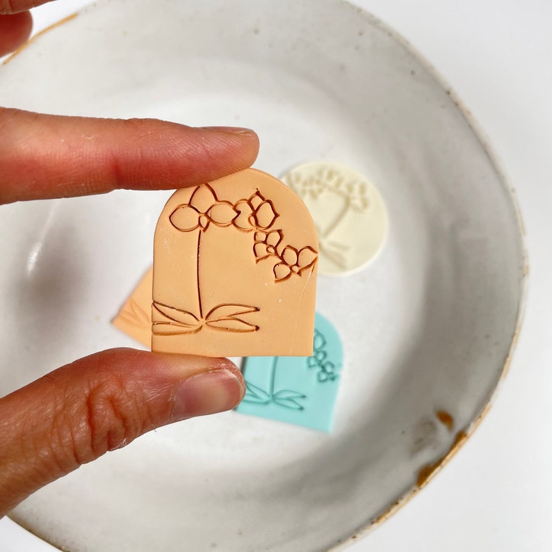 Photo of a polymer clay earring featuring an embossed orchid. At the back is the clay stamp used to emboss the flower.