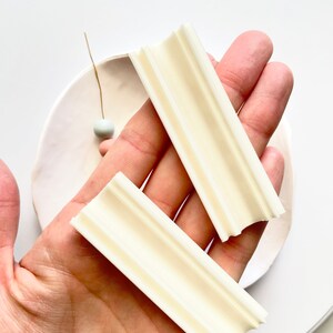 K&ouml;nnte beinhalten: Zwei wei&szlig;e Polymer Clay-Formenwerkzeuge mit rechteckiger Form und gerilltem Design. Die Werkzeuge werden in einer Hand gehalten.