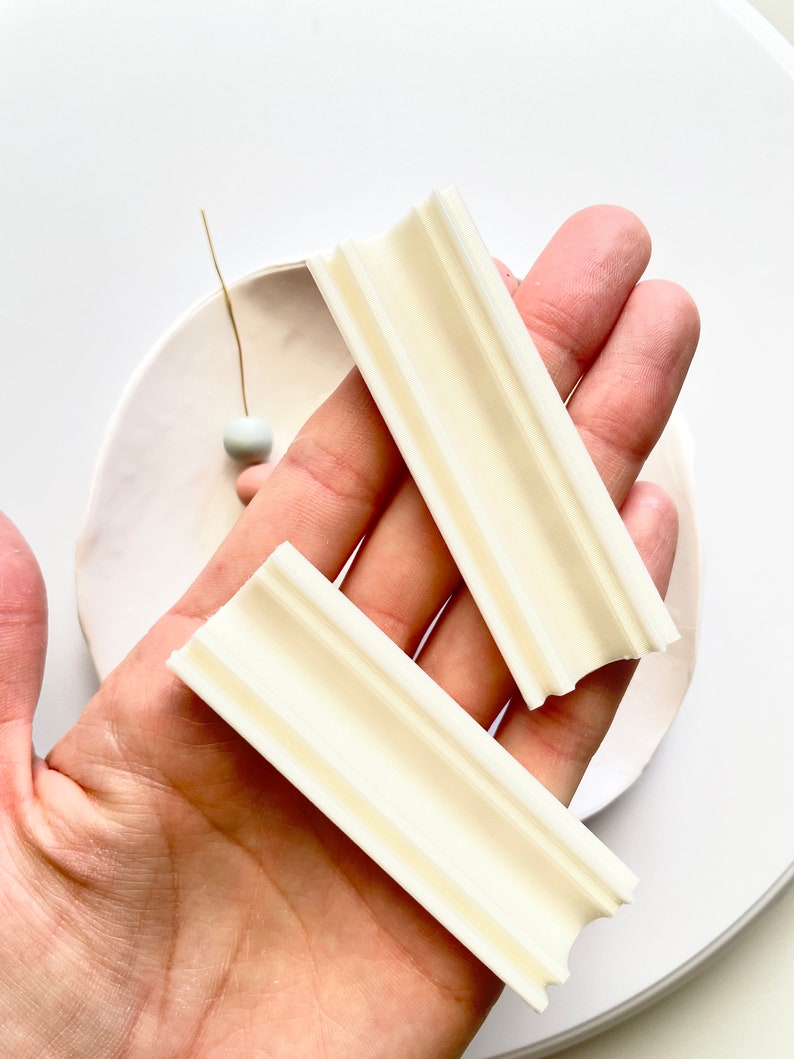 K&ouml;nnte beinhalten: Zwei wei&szlig;e Polymer Clay-Formenwerkzeuge mit rechteckiger Form und gerilltem Design. Die Werkzeuge werden in einer Hand gehalten.