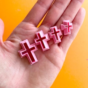 May include: Four pink plastic cross-shaped cookie cutters of varying sizes.