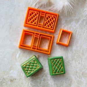 May include: Two green book-shaped charms with gold accents and a diamond pattern, and four orange plastic moulds for making the charms.