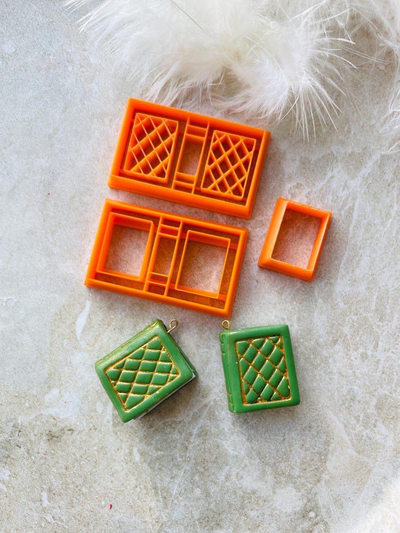May include: Two green book-shaped charms with gold accents and a diamond pattern, and four orange plastic moulds for making the charms.