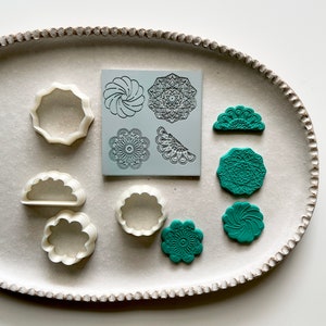 Könnte beinhalten: Ein Set aus weißen Plastik-Ausstechern und grünen Polymer Clay-Formen in Form von Blumen, Wirbeln und geometrischen Mustern. Die Formen befinden sich auf einem weißen ovalen Teller mit einem perlenbesetzten Rand.