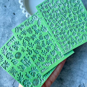 Könnte beinhalten: Drei grüne Silikonformen mit erhabenen Designs aus verschiedenen Blättern und Blumen. Die Formen sind mit "Phoenix & Spruce" und "Gilroy" beschriftet.