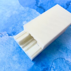May include: White plastic soap dish with three compartments. The dish is on a blue and white watercolor background.