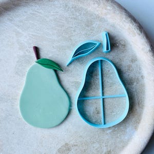 Puede incluir: Un juego de tres cortadores de galletas de plástico azul en forma de pera, hoja y tallo. El cortador de pera tiene un patrón de cuadrícula en el interior.