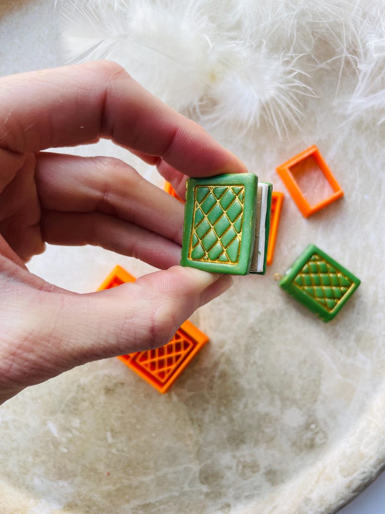 May include: A set of miniature book charms with a green cover and gold accents. The charms are made of polymer clay and have a detailed design. The charms are perfect for adding a touch of whimsy to your jewellery or crafts.
