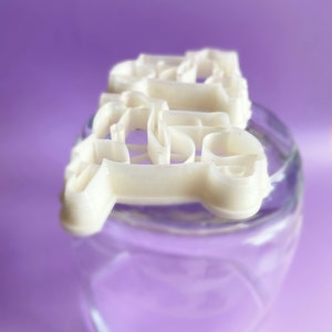 K&ouml;nnte beinhalten: Wei&szlig;e Plastik-Ausstecher in Form des Wortes "LOVE" auf einem durchsichtigen Glasgef&auml;&szlig;.