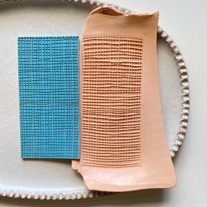 May include: Two rectangular ceramic tiles with a grid pattern. The tile on the left is light blue and the tile on the right is peach.