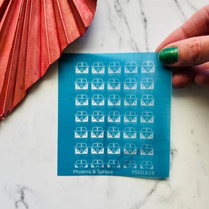 May include: A sheet of blue vinyl with white silhouette images of vintage Volkswagen vans. The sheet is labeled "Phoenix & Spruce" and "PSSILK19".