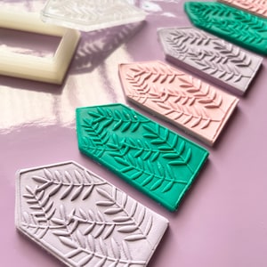 May include: Five different coloured polymer clay house shapes with a leaf design. The house shapes are in shades of green, pink, purple, and grey.