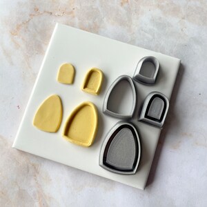 May include: A set of eight polymer clay molds, four in yellow and four in gray. The molds are shaped like arches and ovals.