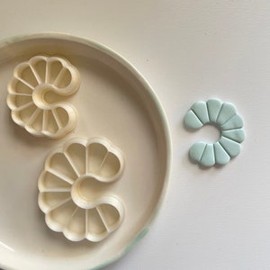 May include: Two white plastic cookie cutters shaped like a crescent moon with scalloped edges, and a light blue clay crescent moon with scalloped edges.