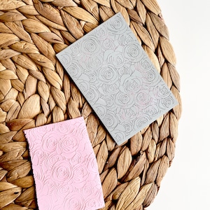 Könnte beinhalten: Zwei Silikonstempel mit Rosenmuster. Ein Stempel ist grau und der andere ist rosa.