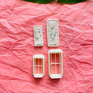 Puede incluir: Cuatro cortadores de galletas de plástico blanco con forma de ventanas. Dos de los cortadores son sólidos y dos tienen un patrón de cuadrícula.