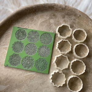 May include: A green silicone mold with 9 different mandala designs. The mold is labeled "METALCLAYSTUDIO" and has the numbers "19" and "30" printed on it. There are 9 white plastic cookie cutters in the shape of mandalas and circles.