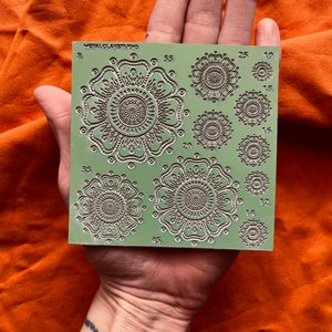May include: A green plastic sheet with 8 different sized mandala designs for crafting. The sheet is labeled "METAL CLAY STUDIO" and has numbers indicating the size of each design.