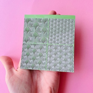 Könnte beinhalten: Eine Platte mit vier Stempeln für Nail Art mit grünem Rand. Jede Platte zeigt ein anderes Design aus stilisierten Blättern.
