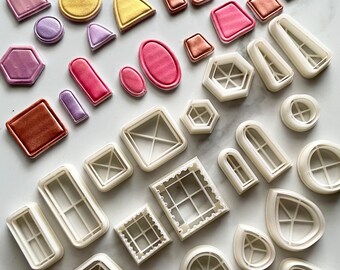 May include: A set of 25 white plastic cookie cutters in various shapes, including arches, windows, and geometric shapes. The cutters are arranged on a white surface.