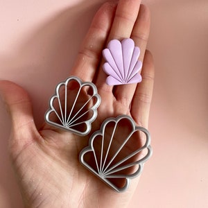 Photo of an Art Deco clay cutter in 2 different sizes, next to a sample of polymer clay earring cut with the same mould. The shape resembles a seashell.