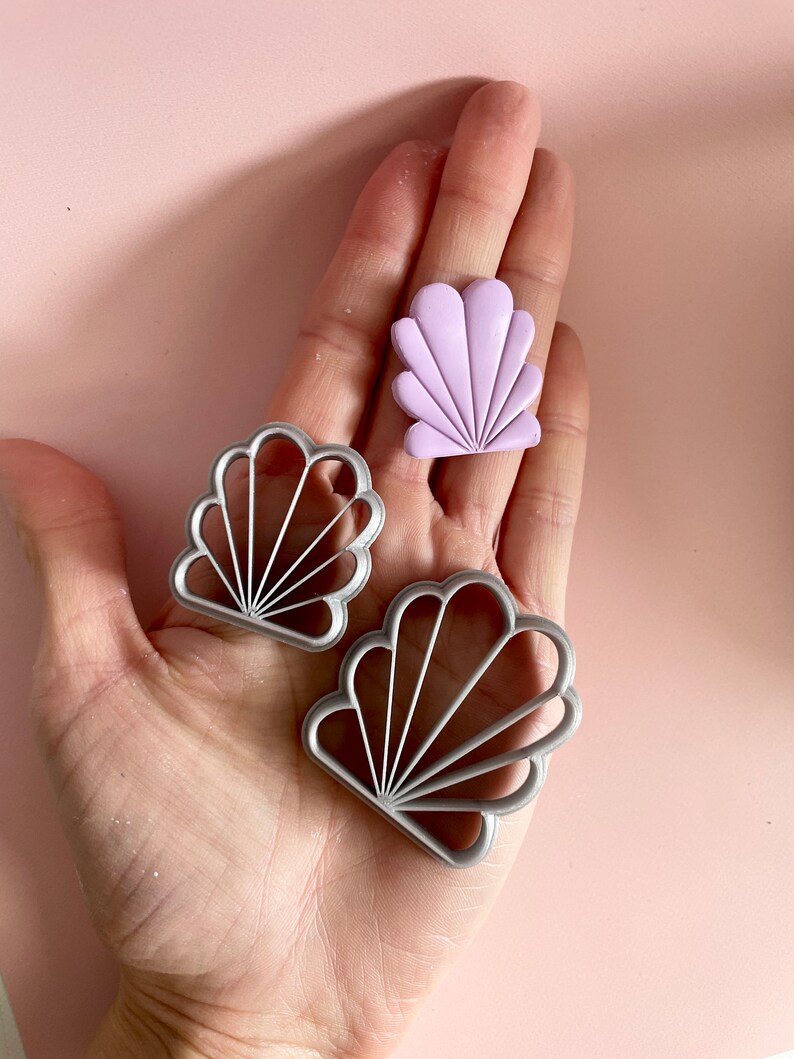 Photo of an Art Deco clay cutter in 2 different sizes, next to a sample of polymer clay earring cut with the same mould. The shape resembles a seashell.