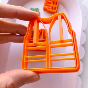 May include: Orange plastic cookie cutter shaped like a safety vest with reflective stripes.