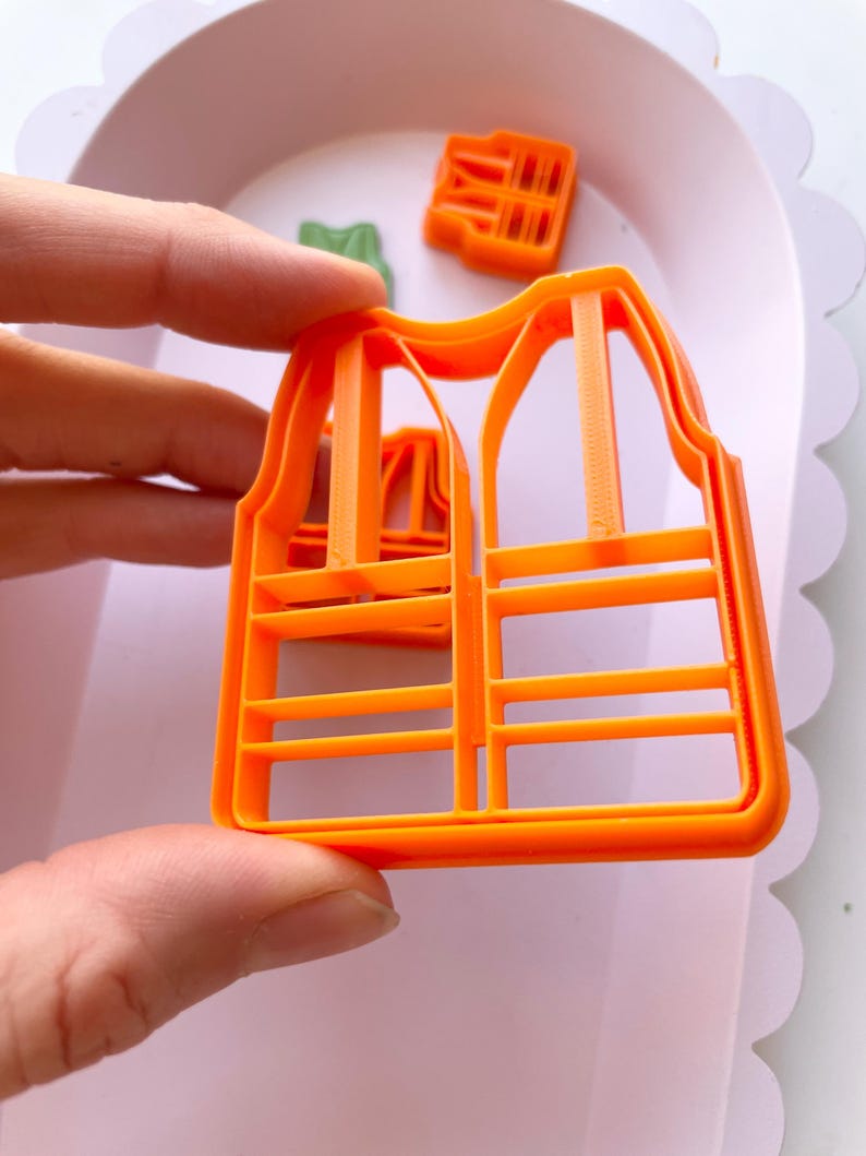 May include: Orange plastic cookie cutter shaped like a safety vest with reflective stripes.