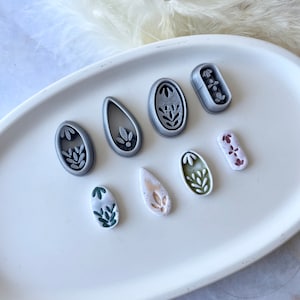 Może przedstawiać: Zestaw ośmiu form do gliny polimerowej z różnymi wzorami kwiatowymi. Formy są w odcieniach szarego, zielonego i białego.