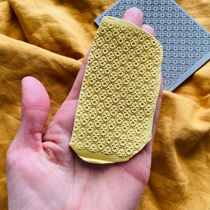 May include: A yellow silicone mold with a geometric pattern. The mold is slightly bent and has a rough texture.