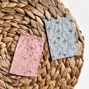 May include: Two pink and gray polymer clay stamps with a geometric flamingo design. The stamps are on a woven straw mat.