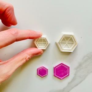 Può includere: Due tagliabiscotti esagonali in plastica bianca e due esagoni di pasta di zucchero viola. I tagliabiscotti hanno un design in rilievo al centro.