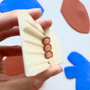 Può includere: Uno stampo in plastica bianca con una serie di scanalature e una piccola apertura. Quattro perline di colore rame sono visibili nell'apertura.