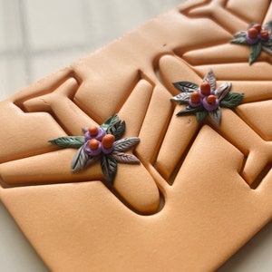 Peut inclure: Gros plan sur un moule en argile orange clair avec trois formes d'avions. Chaque forme d'avion a une petite fleur en pâte polymère avec des accents violets, orange et verts.
