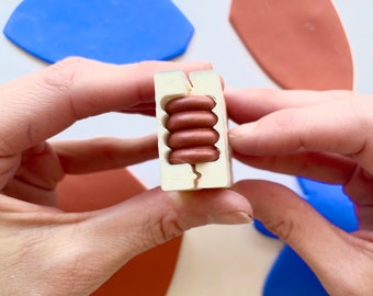 May include: A white mold with a split in the middle, holding a stack of five brown clay beads.