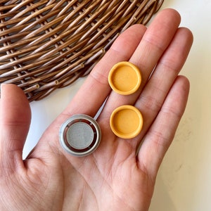 May include: Three small round decorative items. Two are yellow and one is silver with a textured surface.