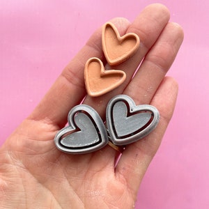 May include: Two pairs of heart-shaped moulds, one pair is peach coloured and the other pair is silver.